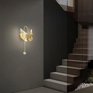 The Swan Wall Light, an elegant indoor lighting fixture from our collection, is tastefully mounted on a dark gray wall adjacent to a modern staircase. This decorative sconce brings sophistication and charm to any contemporary space.