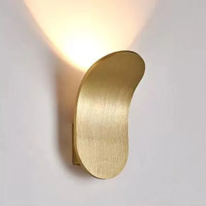 The Curved Wall Light, a Nordic-inspired wall lamp featuring a brushed metal design in gold, emits light upwards and is mounted on a white wall. Perfect for living spaces seeking modern light fixtures that seamlessly blend elegance and functionality.