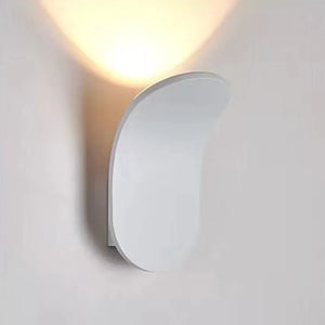 The Curved Wall Light, a Nordic-inspired wall lamp featuring a brushed metal design in white, emits light upwards and is mounted on a white wall. Perfect for living spaces seeking modern light fixtures that seamlessly blend elegance and functionality.