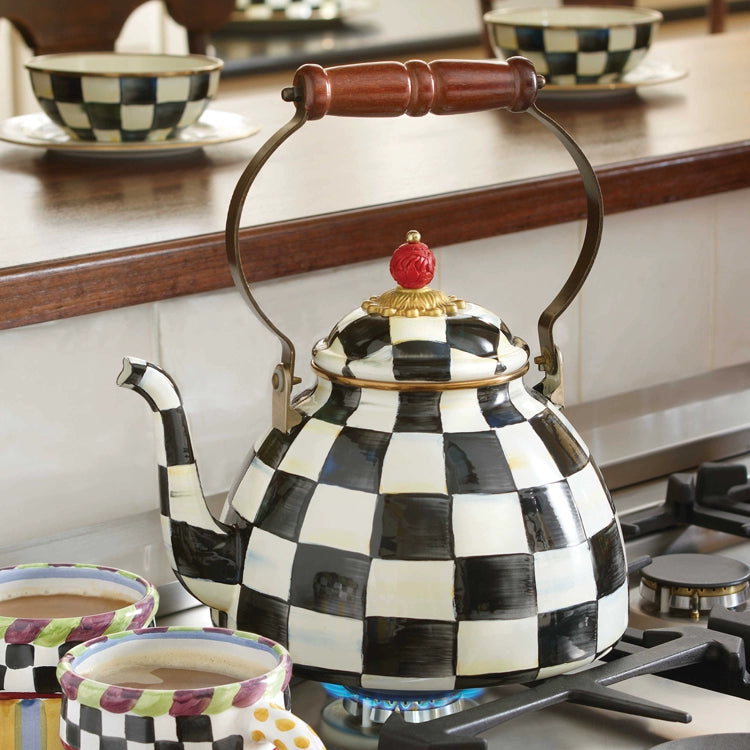 The Vintage Black and White Kettle with a wooden handle warms on a gas stove, its classic checkered design matched by coordinating cups and bowls in the background.