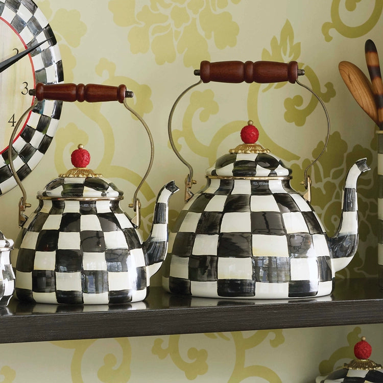 Two Vintage Black and White Kettles with checkered patterns, wooden handles, and red knob lids are displayed on a shelf against a patterned wall. Product shown: Vintage Black and White Kettle.