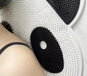 Close-up of a shoulder against the Panda Shower Massage Mat, featuring a textured white surface with black circular patterns resembling acupuncture points to enhance circulation.