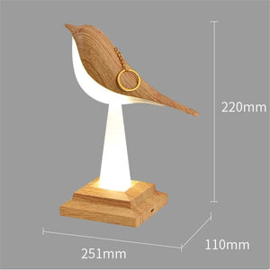 A Bird Table Night Light, featuring a wooden and white sculpture of a bird on a stand, is shown with dimensions: 220mm height, 110mm width, and 251mm length. A small, round object, possibly a ring, is attached to the bird's head. Its minimalist design makes it perfect for your living space.