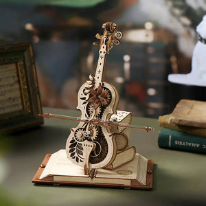 The Cello Puzzle Music Box is a detailed wooden model reminiscent of a violin, featuring intricate gears and embellishments, displayed on an open book placed on a tabletop.