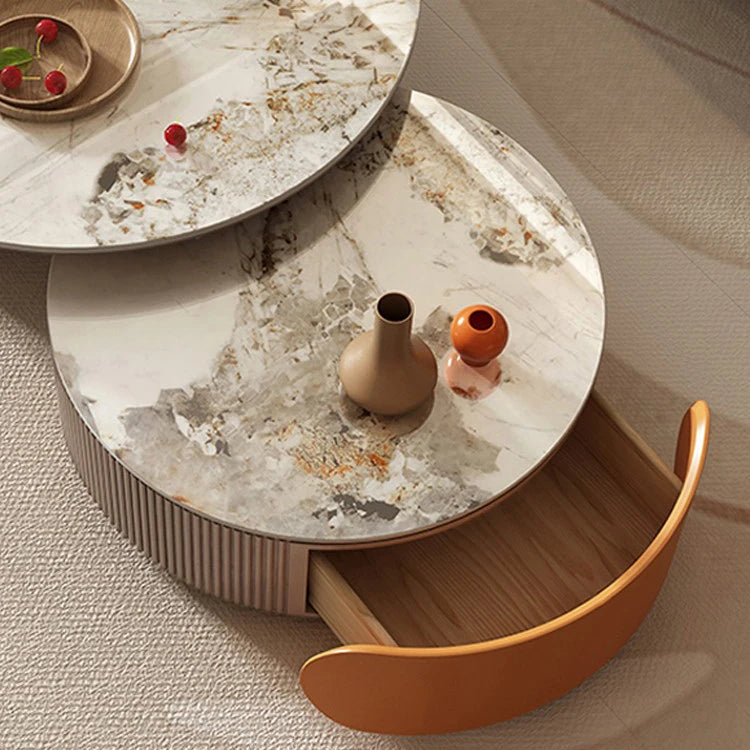 The Luxe Round Coffee Table set features two nesting round tables with abstract marble patterns: the lower table includes a partly open drawer holding two vases, while the upper sintered stone table displays a tray with red berries.