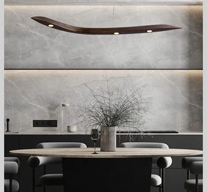 A modern dining area with a round table, gray chairs, a vase of dry branches, and the Spiral Wood Pendant Light brings warmth and elegance to the gray marble wall backdrop.