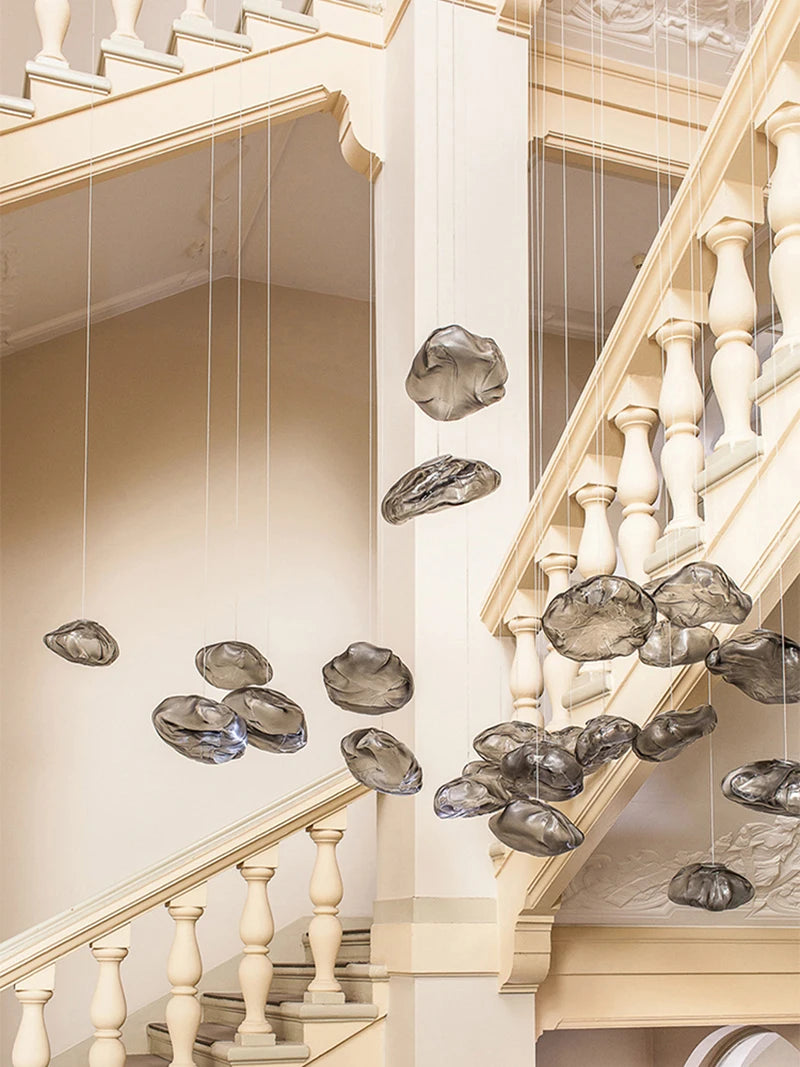 Luxe Cloud Glass Pendant Lights, featuring irregular translucent glass forms, hang on wires in the stairwell of a cream-colored interior with ornate railings.