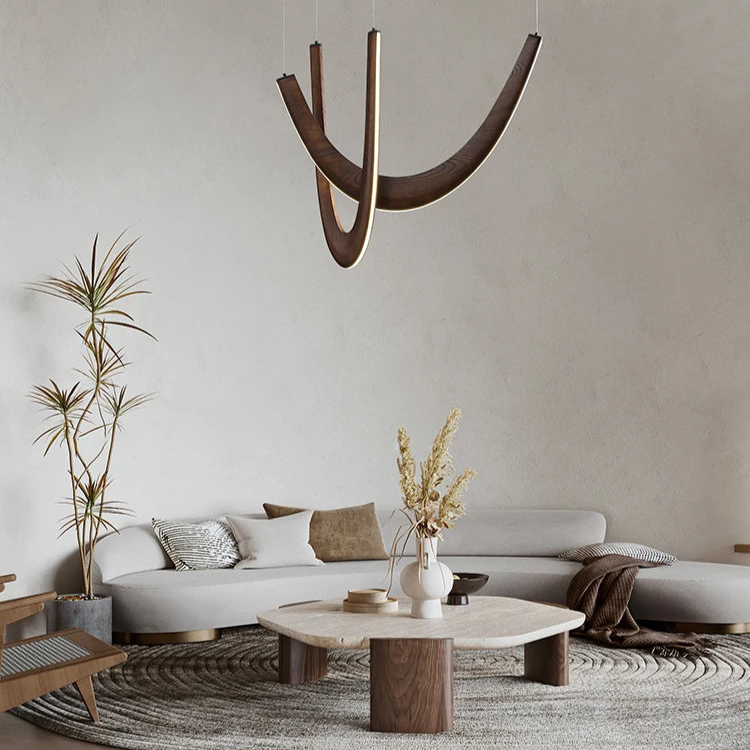 Minimalist living room featuring a curved gray sofa, geometric wooden coffee table, the Double Curve Wood Pendant Light as a modern accent, neutral-tone decor, and a potted plant in the corner.
