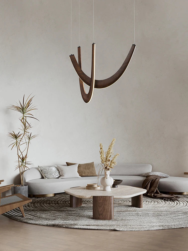Modern living room with a Double Curve Wood Pendant Light, round coffee table, light gray sectional sofa, neutral decor, potted plant, and textured circular rug on a light wooden floor.