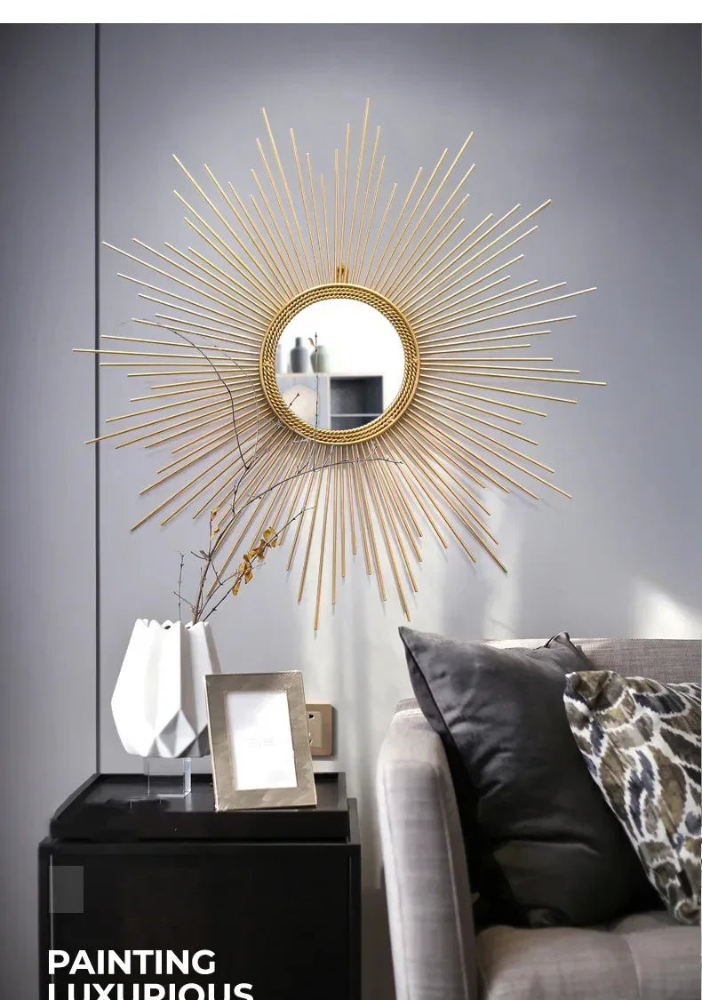 A Luxe Sunray Wall Mirror hangs on a gray wall above a black side table with a white vase, framed photo, and a gray couch with patterned pillows, creating a stylish statement in the space.