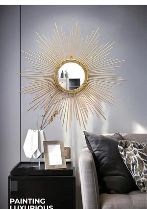 A Luxe Sunray Wall Mirror hangs on a gray wall above a black side table with a white vase, framed photo, and a gray couch with patterned pillows, creating a stylish statement in the space.