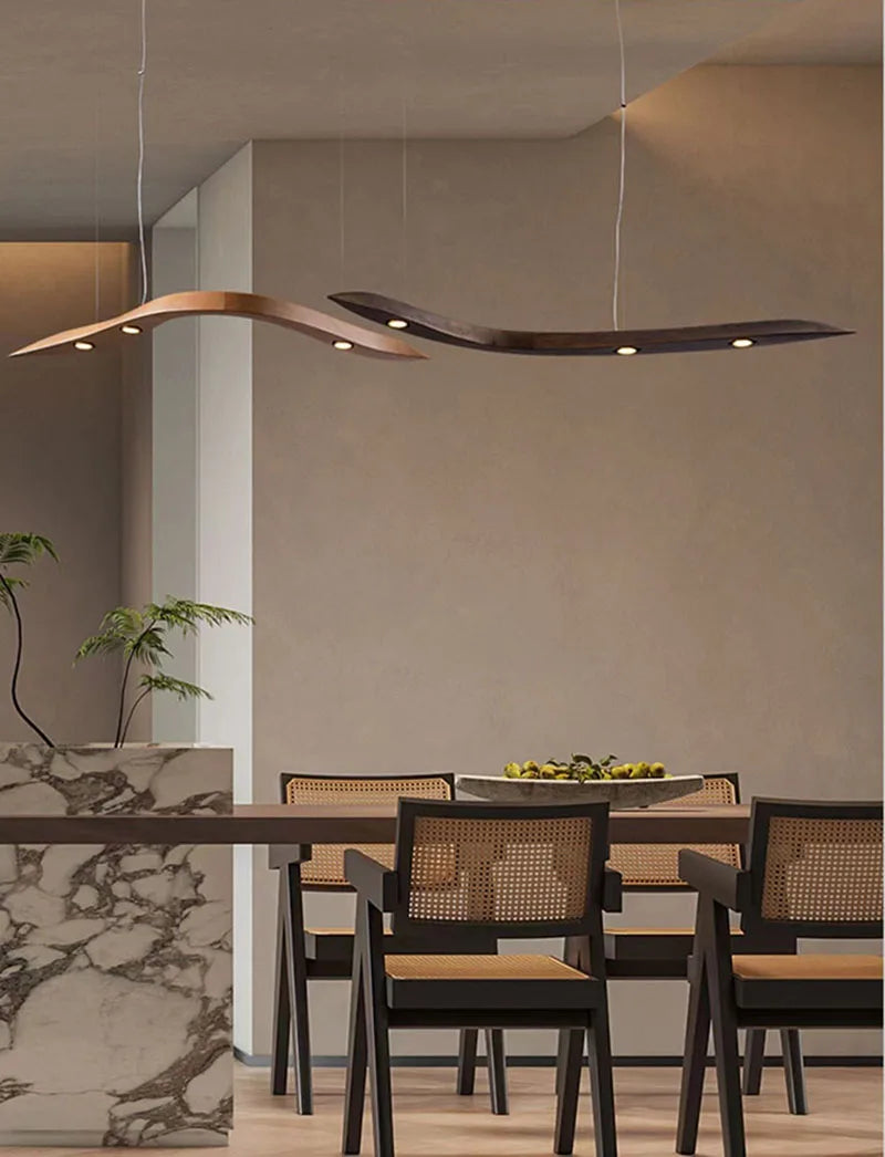 Modern dining area featuring a marble-topped table, six woven-back chairs, and a fruit bowl centerpiece, illuminated by two Spiral Wood Pendant Lights from Organic Modern Lighting.
