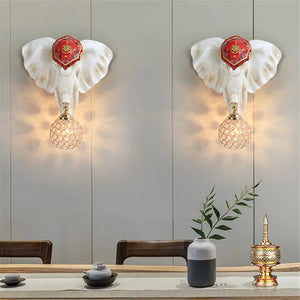 Two 3D Elephant Wall Lights with glowing bulbs, adding a unique ambiance, are mounted on a light-colored wall above a table set with a vase, cups, and a decorative container.