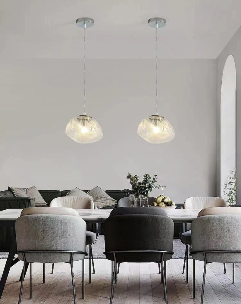 A modern dining room with a white table, mixed gray chairs, the Luxe Cloud Glass Pendant Light, a dark sofa, and decorative plants.