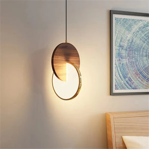 The Dual Disc Pendant Light, with its modern circular geometric design featuring wood and illuminated segments, hangs near a framed abstract artwork and wooden bed frame, enhancing the sophisticated home aesthetic.