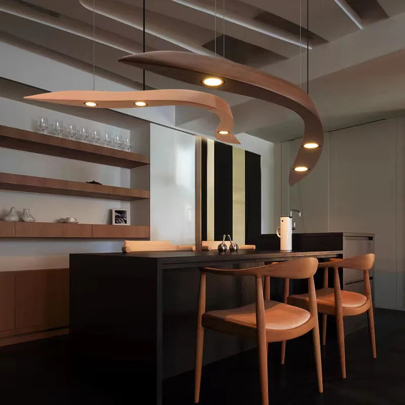 Modern kitchen with dark cabinetry, wooden chairs, and the Spiral Wood Pendant Light above the dining table; open shelves with glassware line the wall, highlighting stylish modern home lighting.