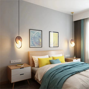 A modern bedroom features a wooden bed with teal and yellow bedding, flanked by two side tables. The Dual Disc Pendant Lights elegantly illuminate abstract wall art on the light gray wall, exuding a sophisticated home aesthetic.