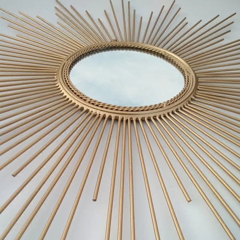 The Luxe Sunray Wall Mirror features a round gold design with a sunburst frame of radiating metal rods, creating a striking statement in any space, especially against a plain background.