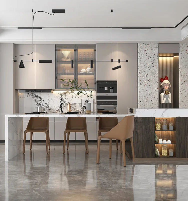 A modern kitchen features a marble island and brown chairs with sleek cabinetry. Modern Track Lighting with adjustable heads hangs above, while a decorative statue sits on the right. Marble floors enhance the clean design, offering an industrial-inspired ambiance.