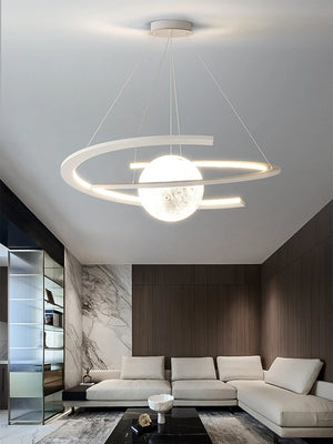 A modern living room showcases a beige sectional sofa under the elegant Moon Trajectory Pendant Light. Marble accents complement a black coffee table, and LED technology ensures both energy efficiency and sophistication.