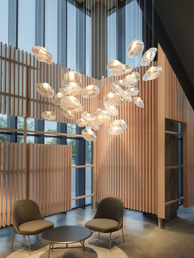 A modern lobby showcases two chairs, a round table, and Luxe Cloud Glass Pendant Lights overhead, set against floor-to-ceiling windows and vertical wooden slats in the background.