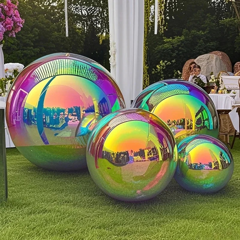 Four large Inflatable Gazing Balls display stunning iridescence on the grass at an outdoor event, serving as eye-catching garden decor among tables, decorations, and guests reflected in their surfaces.