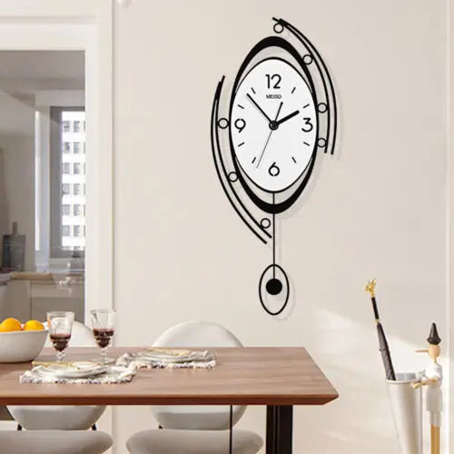 The Zen Arc Oval Statement Clock, featuring black abstract ovals and lines, is mounted on a white wall above a dining table set with glasses, bowls, and a fruit bowl.