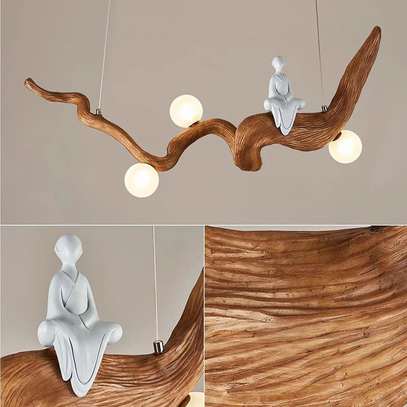 The Zen-Inspired Wooden Pendant Light features spherical bulbs and a sculpted figure seated on a branch-like structure. The close-up showcases the natural wood texture and intricate details, creating a tranquil Zen aesthetic.