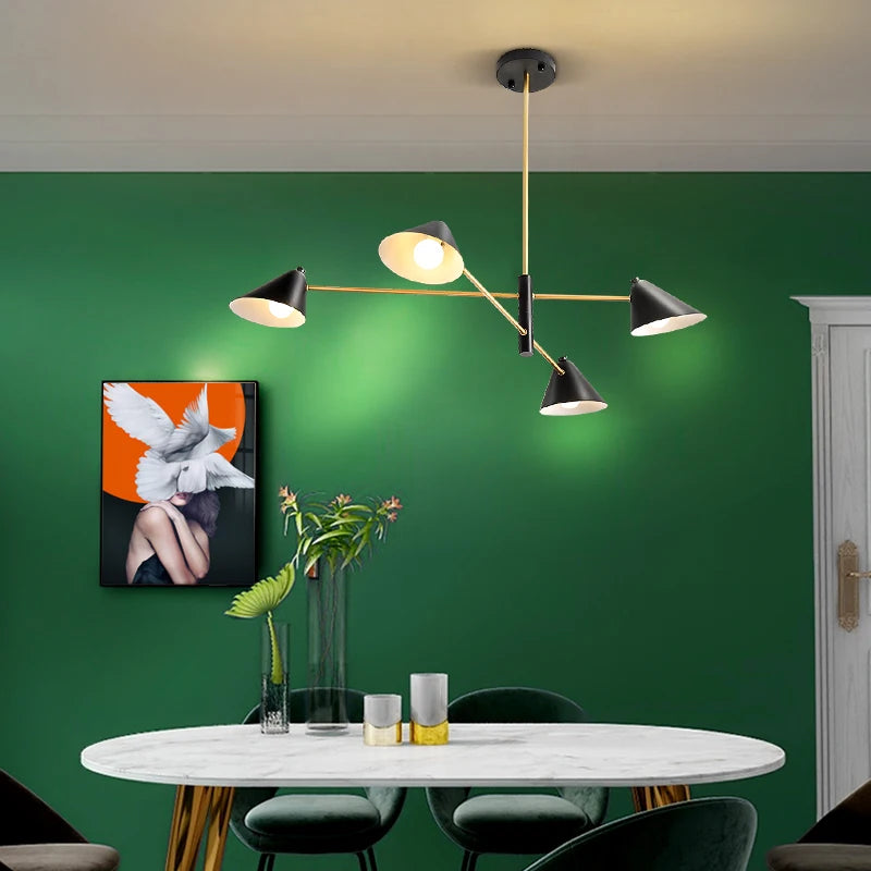 A modern dining room features a green wall, a round white marble table with four chairs, and an elegant Multi-Arm Ceiling Light in black and gold. Abstract wall art enhances the minimalist decor, including a glass vase with leaves.