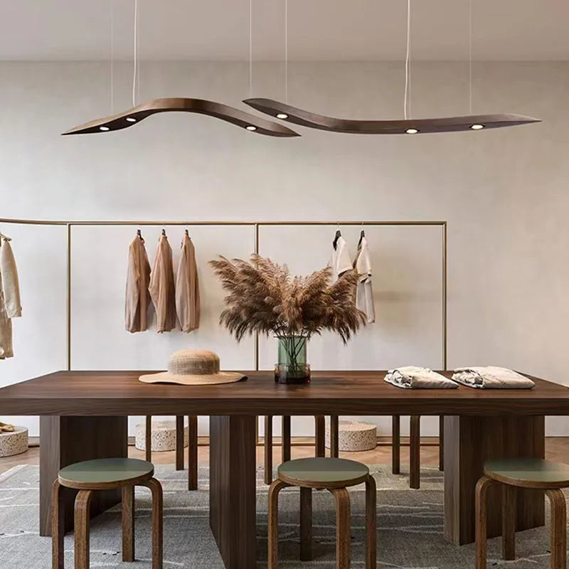 Minimalist dining area featuring a wooden table, stools, decorative vase with pampas grass, hanging garments, and a Spiral Wood Pendant Light for organic modern lighting.