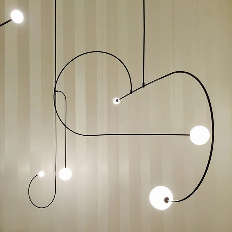 The Minimalist Line Light, featuring curved black metal rods and spherical white lights, elegantly complements a striped beige wall to showcase modern design.