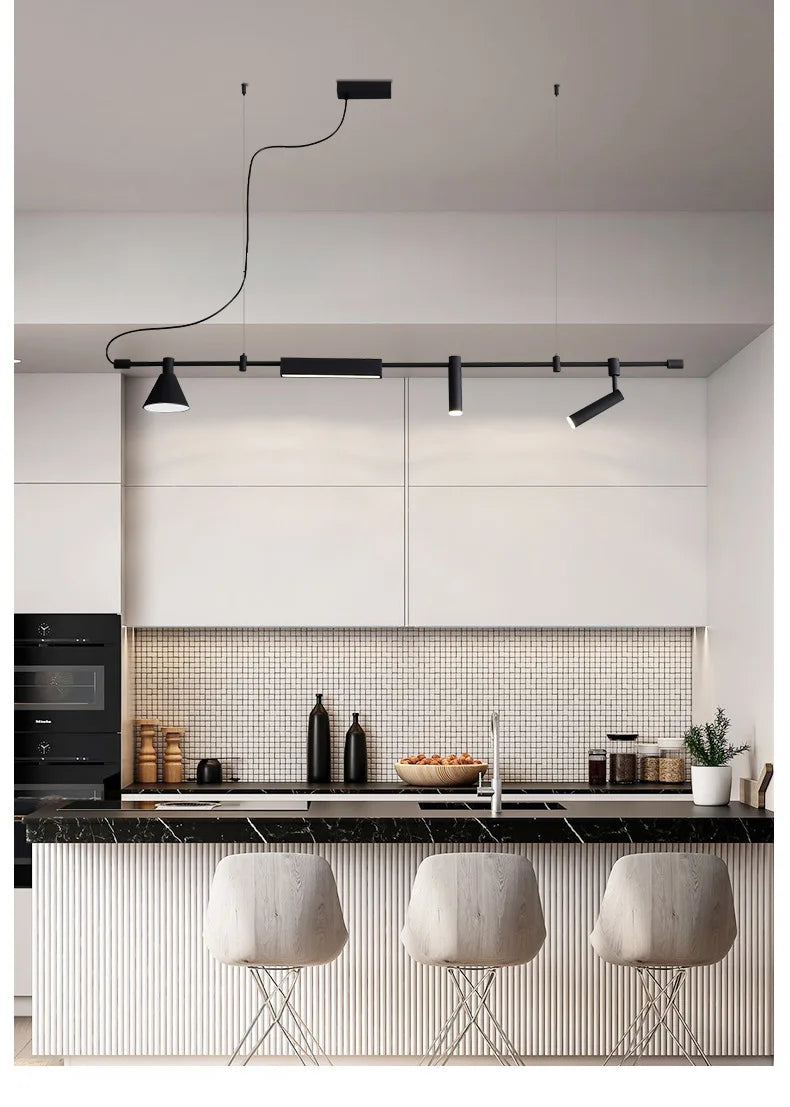 A modern kitchen showcases a sleek island with three stools and industrial pendant lighting. The tile backsplash and neatly organized counter enhance the look. Modern Track Lighting with adjustable heads ensures optimal illumination throughout the space.