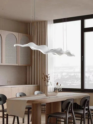 A modern dining room showcases a wooden table, neutral-toned chairs, and the Leaf Pendant Light, casting a warm glow. A large window offers a city view, enhancing the serene ambiance.