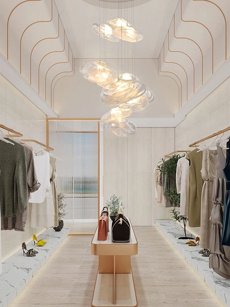 Modern walk-in closet featuring hanging clothes on both sides, a central bench with handbags, light wood flooring, and the Luxe Cloud Glass Pendant Light—creating a striking yet elegant atmosphere.