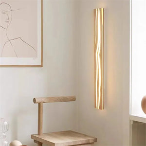 The Rectangle Wood Wall Light elegantly illuminates the space next to an organic wooden chair, while a minimalistic line art picture above adds sophistication to the wall.