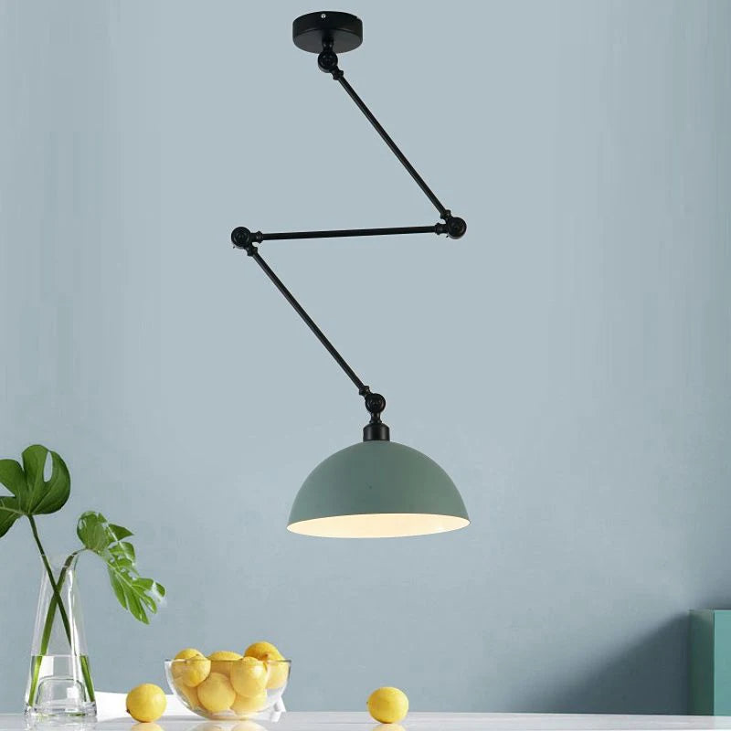 The Zig Zag Pendant Light in sleek black, with its adjustable arm system, elegantly hangs over a table decorated with lemons and a vase of green leaves. A soft light blue wall serves as the backdrop, enhancing the industrial design appeal.