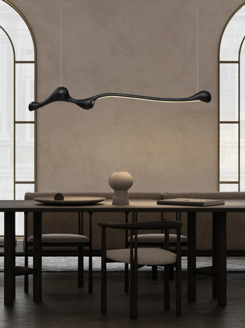 A modern dining room features the Tideform Biomorphic Pendant Light as a sculptural LED fixture, above a minimalist table setting with neutral walls and arched windows, capturing the essence of Nordic minimalism.