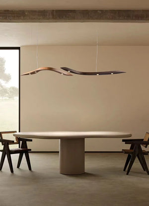 Minimalist dining area featuring an oval table, two wooden chairs, and a Spiral Wood Pendant Light hanging from the ceiling. A large window fills the space with natural light.