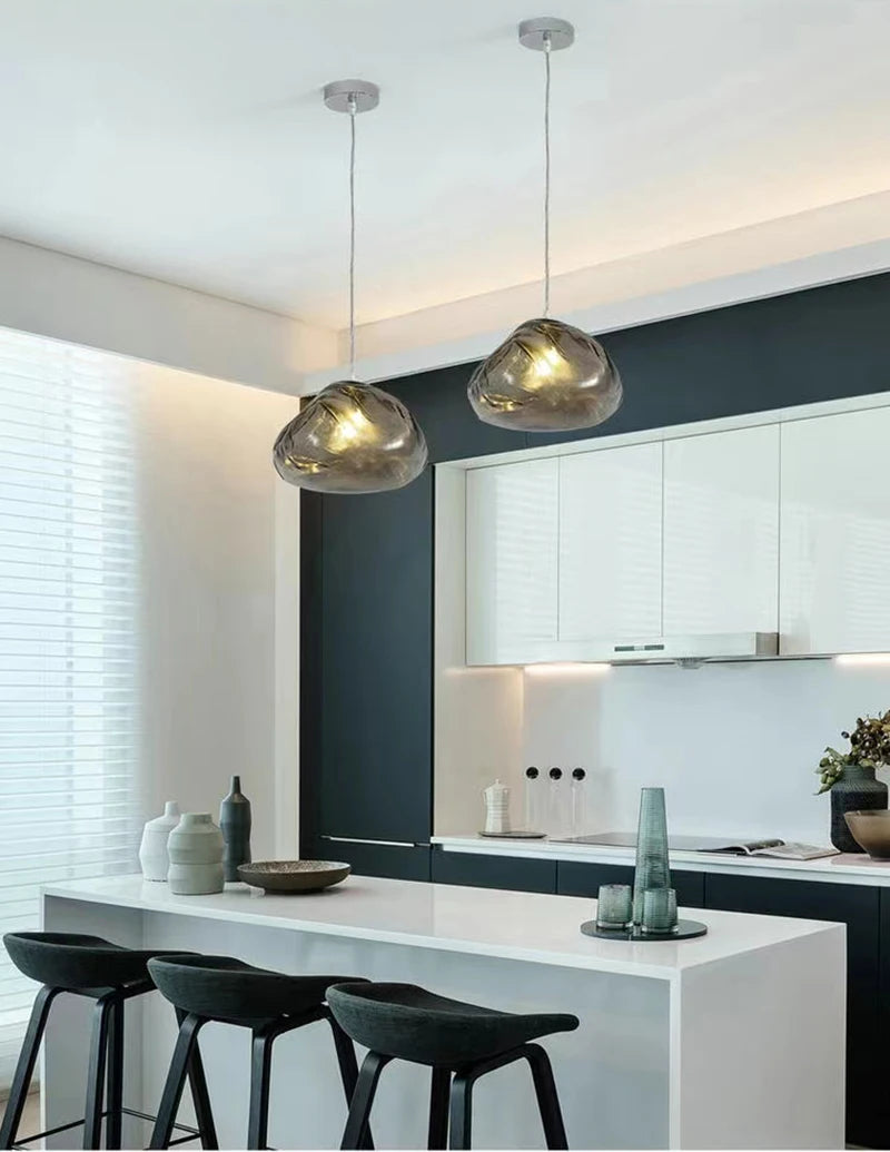 Modern kitchen with a white island, three black barstools, decorative vases, and two Luxe Cloud Glass Pendant Lights hanging above the counter.