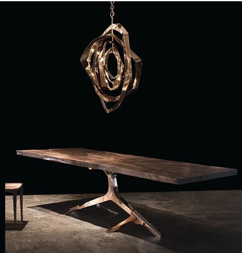 A modern wooden table with a sculptural metallic base is paired with the Elegant Industrial Gallery Pendant in rose gold, set against a dark background.