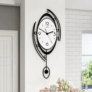 The Zen Arc Oval Statement Clock, featuring a white face, black numbers, and an abstract black frame, hangs on a white wall above flowers to add a modern touch to your décor.