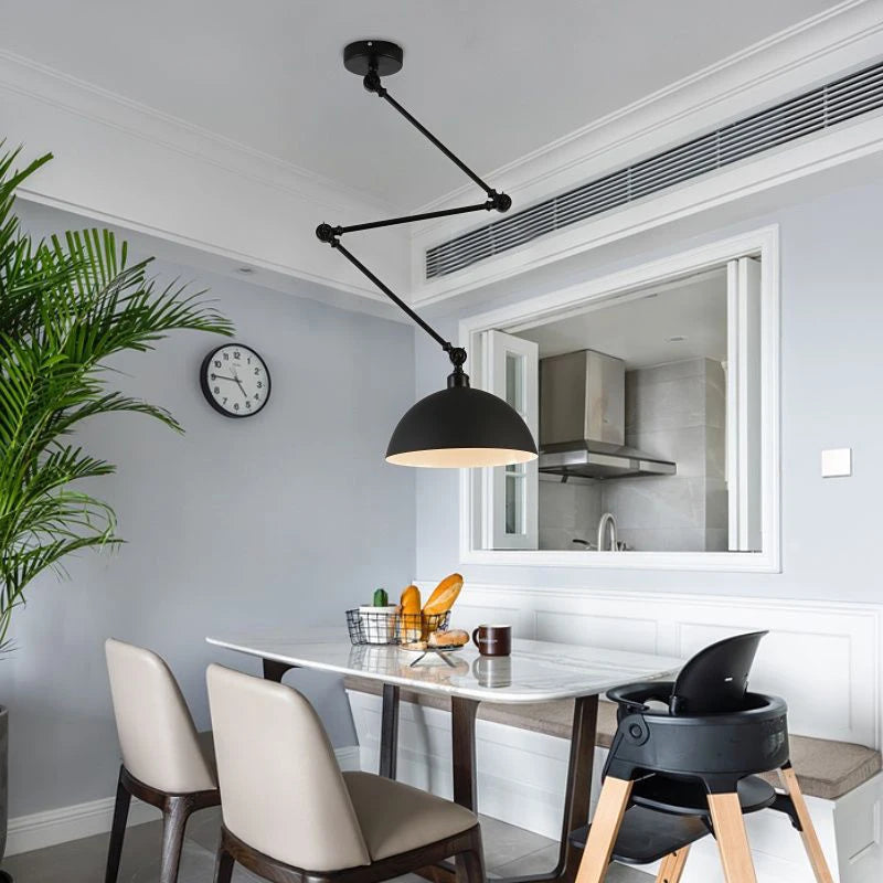 The modern dining area boasts a table with four chairs, a high chair, and a fruit basket under the striking Zig Zag Pendant Light. An industrial touch is added with the large black lamp overhead. A wall clock and potted plant complete the decor as the kitchen peeks through the window.
