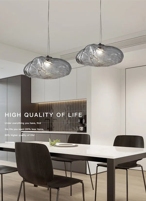 Modern dining room with a white table, four dark chairs, and Luxe Cloud Glass Pendant Lights overhead. Minimalist kitchen cabinets in the background complete the look. Text about high quality of life is overlaid on the image.