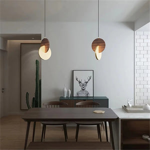 A dining room featuring a wooden table, four chairs, and a Dual Disc Pendant Light. The sideboard is adorned with a framed deer illustration and accompanied by a cactus. The minimalist decor adds to the home’s sophisticated aesthetic.