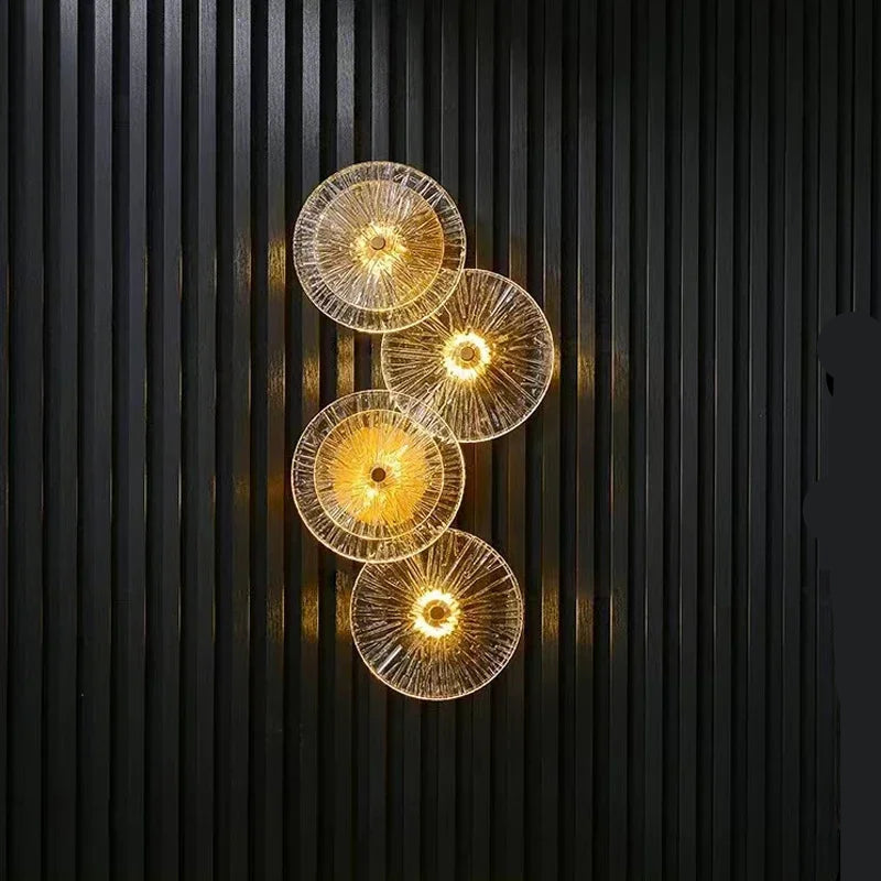 Four Amber Deco Wall Sconces with glass discs are illuminated and vertically arranged on a dark, striped wall, adding a modern touch with their LED design.