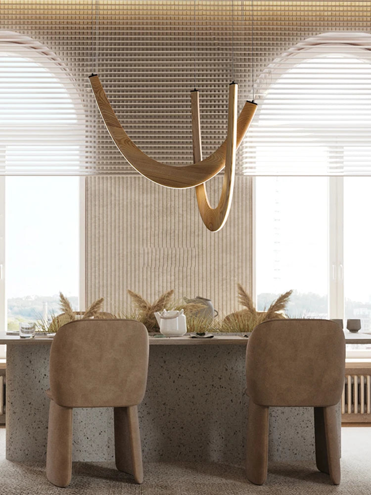 A modern dining area features two beige chairs at a stone table, decorative dried plants, and a Double Curve Wood Pendant Light, set against large windows with horizontal blinds.