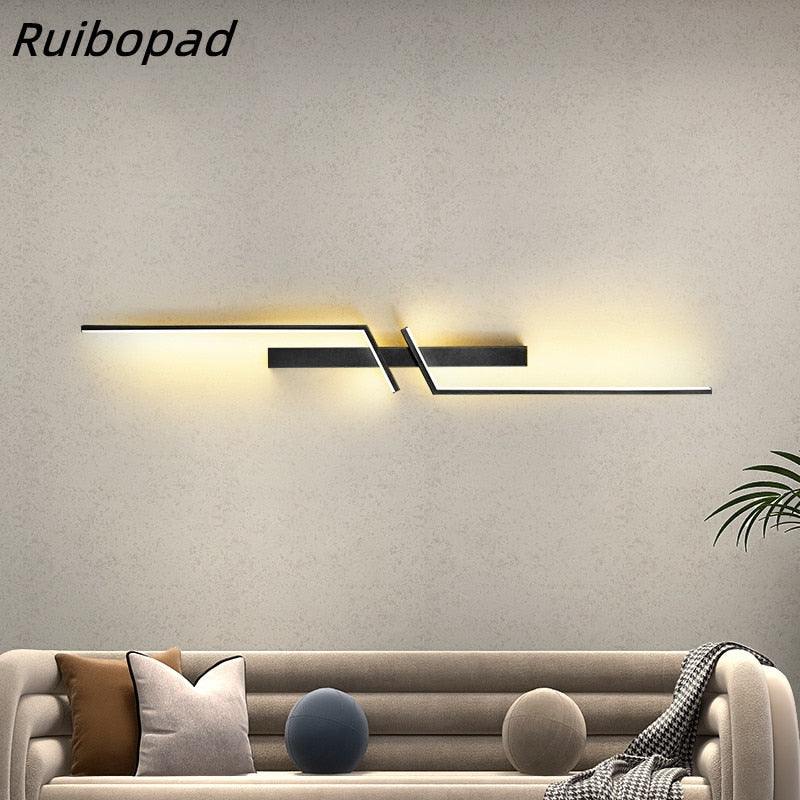 The Minimalist Wall Sconce, with its modern geometric LED design, is mounted above a beige sofa with assorted pillows; a decorative plant sits on the right.