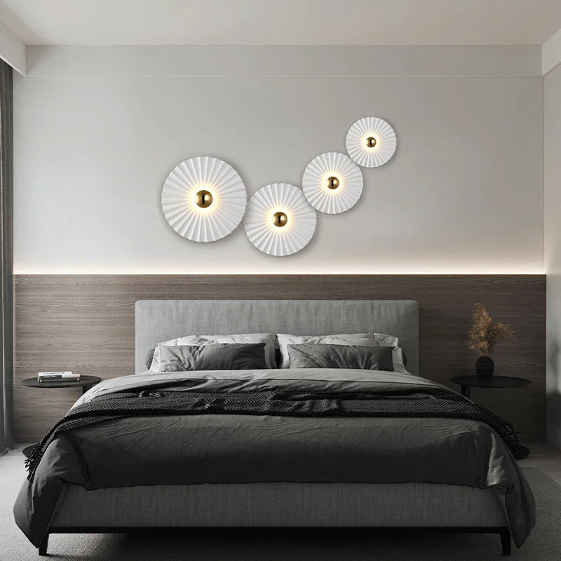 A modern bedroom featuring a gray upholstered bed, wooden accent wall, minimalist bedding, and four Origami Circle Wall Lights arranged above the headboard.