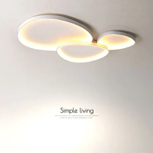 The Nordic Minimalist Ceiling Light, with its three overlapping circular panels, emits a warm glow and has dimmable brightness. The text "Simple living" underscores its sleek design and customizable color temperature for a tailored ambiance.