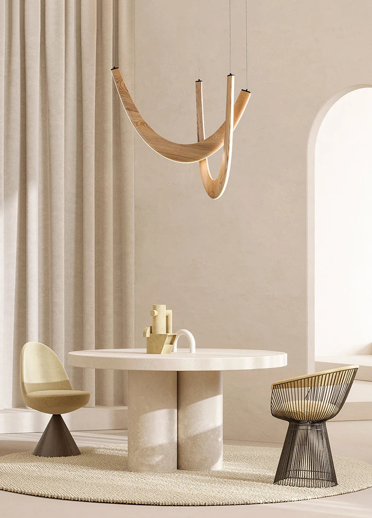 A modern dining area featuring a round table, two contemporary chairs, the Double Curve Wood Pendant Light, and neutral-toned decor.